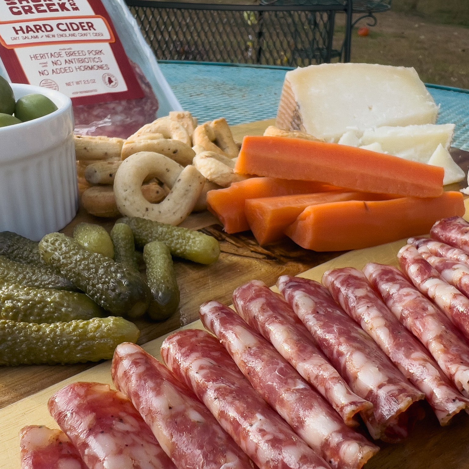 Platter of meats, cheeses, and vegetables on a wooden board with a bottle of hard cider in the background.